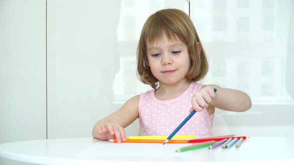 Portrait of Little Child Girl Draws with Pencils Sitting at Table at Home