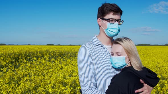 Young Couple Hugging in a Field in Protective Masks alt
