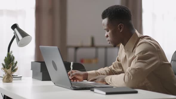 Young Black Man is Viewing and Listening Online Learning Webinar on Laptop Selfeducation at Home alt