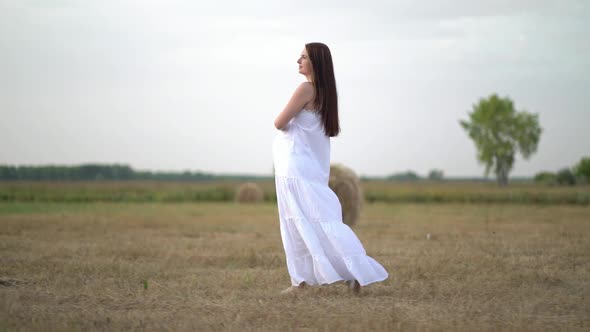 Beautiful Pregnant Woman in Wheat Field with Haystacks at Summer Day alt