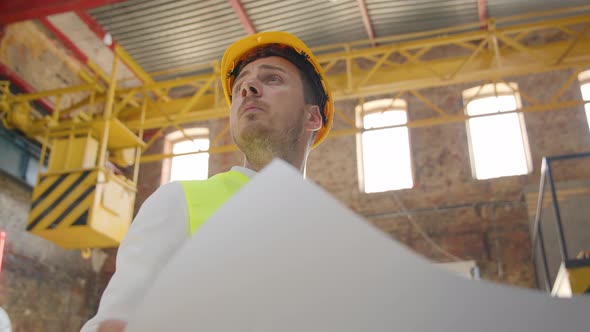 Young Man Engineer Inspection of a Row with Drawings in His Hands alt
