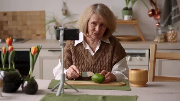 An Elderly Female Food Blogger Showing Ingredients and Explaining an Avocado Recipe on Her Phone alt