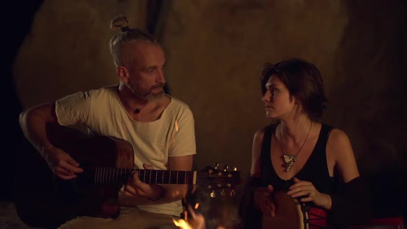 Friends Speaking Smiling Playing on Instruments Sitting Near Bonfire at Night Beach alt