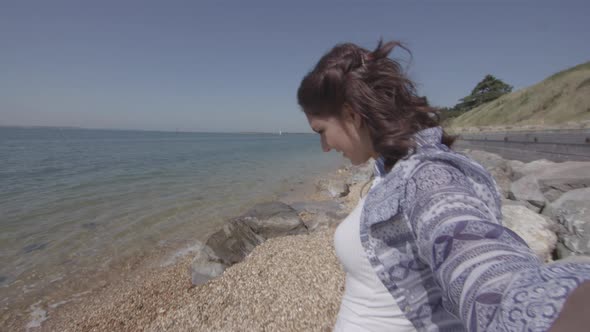 POV Shot Of Young Woman Reaching Down To Pick Up Plastic Bottle On Beach - Ungraded alt