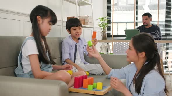 Happy Asian family, mum, and kids play with colorful toys together on a sofa.