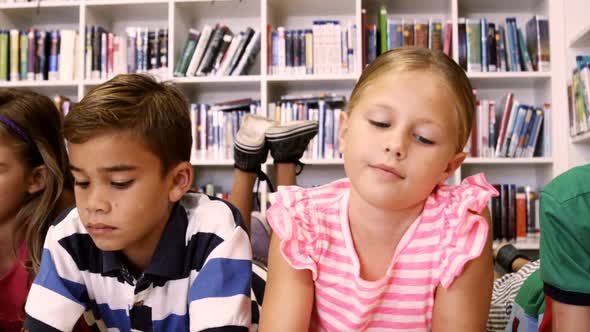 Teacher and kids lying on floor reading book in library alt