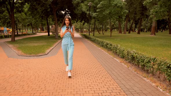 Young Caucasian Woman Happy About Great News Walking on the Street in City Park alt