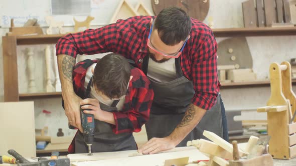 Handsome Father and His Teen Son Working with Drill at Workshop