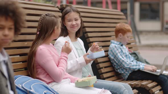 Two Schoolgirls Having Bite Together Outdoors alt