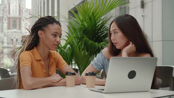 Two Young Mixed Race Girls Have Cute Conversation While Sitting Outdoors in a Summer Cafe of the alt