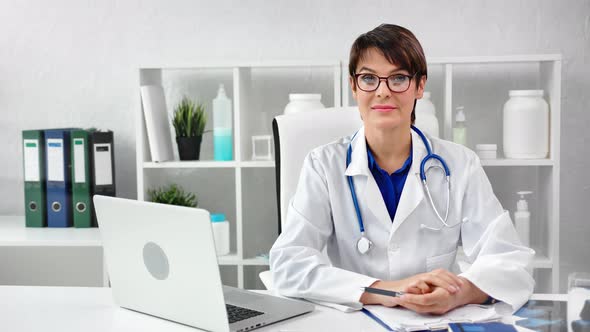 Portrait Smiling Mature Female Doctor in Uniform Wearing Glasses Posing at Modern Workplace alt