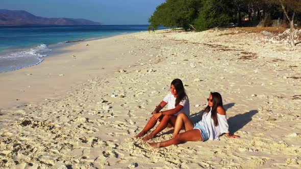 Female models tanning on tranquil coastline beach adventure by clear sea and white sandy background  alt