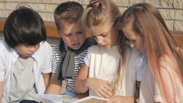 Cute kids reading a book outdoors alt