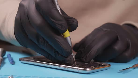 The Master Unscrews the Bolts on the Smartphone with a Screwdriver
