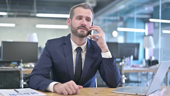 Cheerful Businessman Talking on Smartphone in Office alt