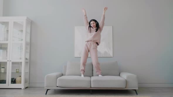 Young woman wearing wireless headphones dancing and singing alone in living room