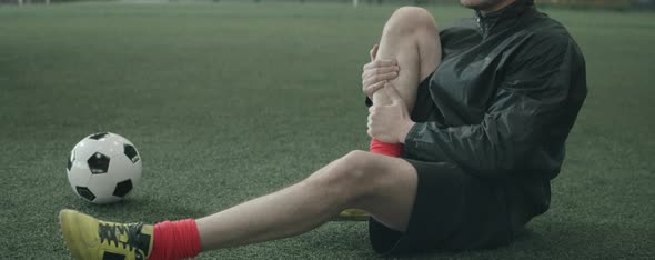 Football Player Stretching Legs on Indoor Field alt