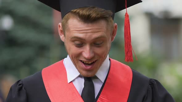 Surprised Male Graduate Looking Down With Smile on Face, Career Opportunity alt