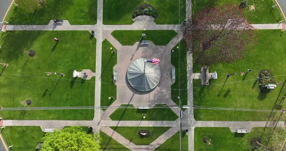 American flag waving in breeze in town center. Aerial reveals traffic circle roundabout in small tow alt
