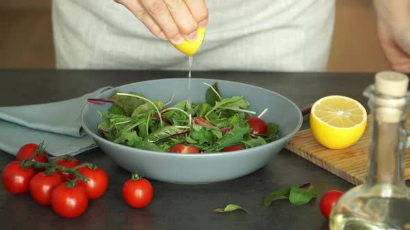 Female Hands Squeeze Lemon Juice Into Green Salad of Tomatoes and Fresh Lettuce Leaves