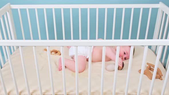 Happy infant baby boy lying in the crib, studio blue background. Smiling child in white diaper