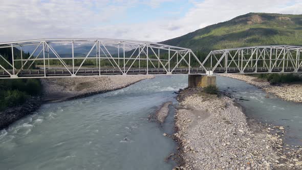 Drone flight under a bridge across the turquoise waters of the Toad River in British Columbia, Canad alt