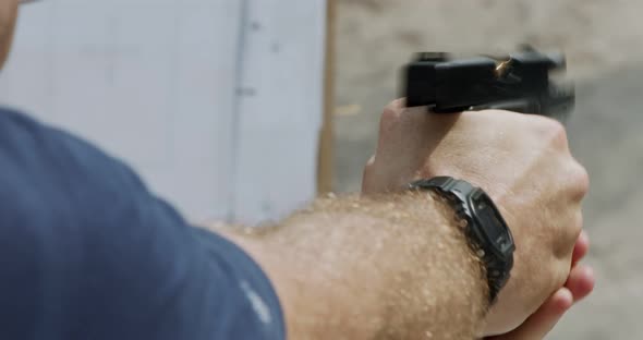 Slow motion close up shot of a man shooting a hand gun while moving backwards