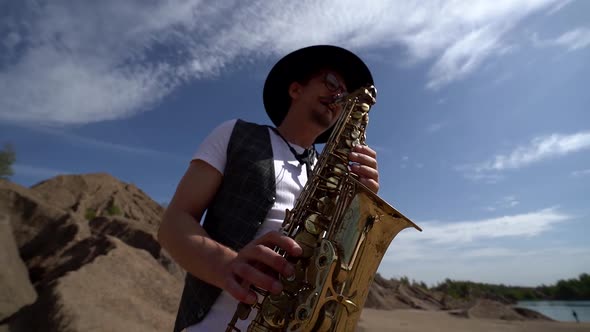 Close-up of a Musician in a Hat Playing Jazz on a Saxophone Standing in the Desert Against a alt