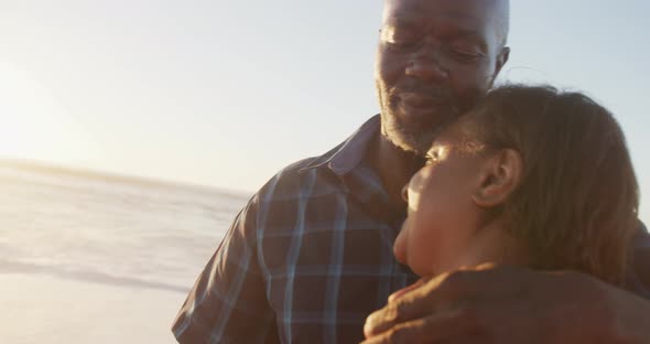 Smiling senior african american couple holding hands and dancing on sunny beach alt