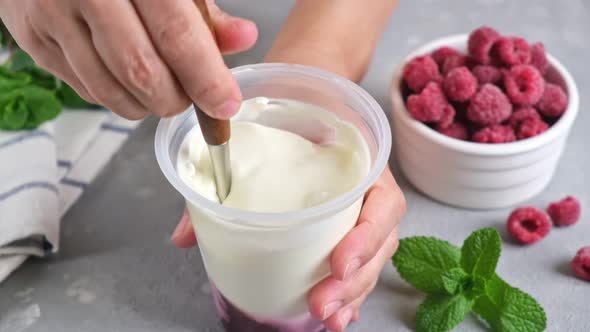 Greek yogurt in jar. Person stirring berry filling with natural greek yogurt in plastic jar