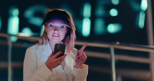 Positive Woman Scrolling Apps on Her Smartphone on Streets of Night Town alt