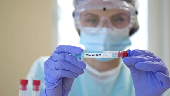 Professional Female Scientist Wearing Glasses and a Mask Holds a 2019Ncov Coronavirus Vaccine Sample alt