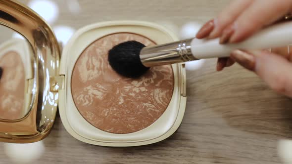 Makeup brush in a container with beige face shadows powder alt
