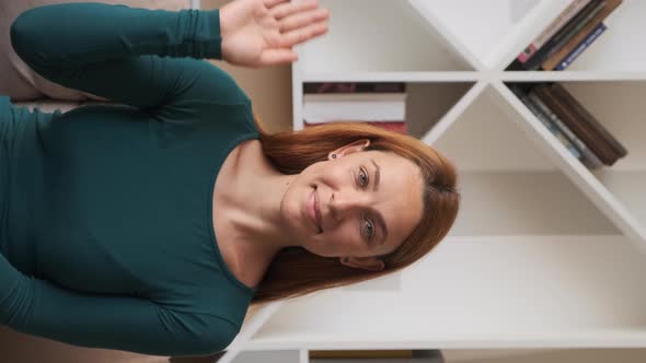 Beautiful Young Woman Having Video Chat Using Webcam at Home Waving Hand. Vertical Screen.