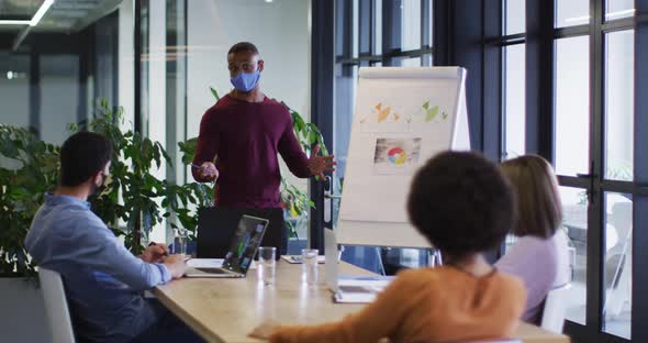 Diverse business people wearing masks sitting listening to a presentation in office alt