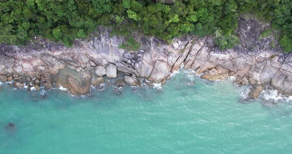 Top view empty coastal sea through forest towards rocky cliff coastline during sunset.