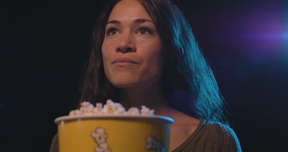 Woman watching a movie at the cinema, she is eating popcorn and smiling