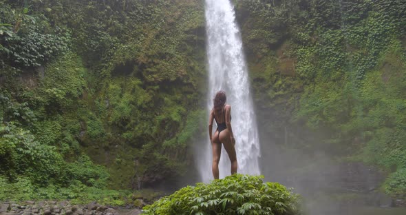 Exotic Shot of Elegant Female Model Standing Against Magnificent Waterfall alt