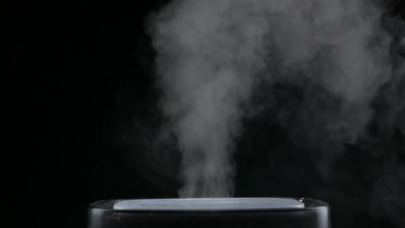 Mist from a black electric humidifier & oil diffuser in a dark room