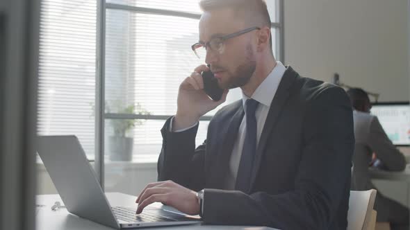 Businessman Talking on Phone and Using Laptop in Office alt