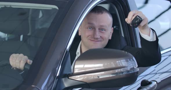 Portrait of Chubby Caucasian Man Bragging Car Keys at Camera and Smiling. Happy Owner Sitting in alt