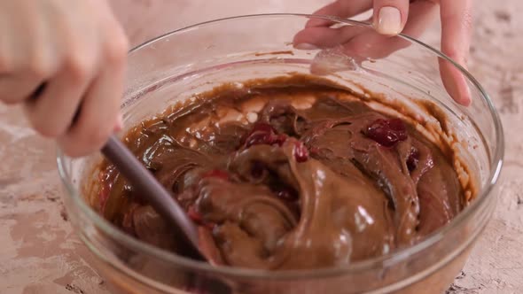 Female hands fold the cherries into chocolate batter.