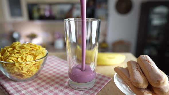 Pouring fresh berry smoothie into a transparent glass on a rotating table alt