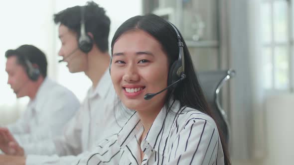 A Woman Of Three Asian Call Centre Agents Looking Up From Computer And Smiling To Camera alt