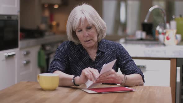 Senior adult woman opening bills at home on kitchen table