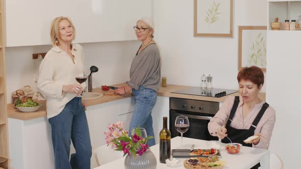 Three Mature Girlfriends Drinking Wine and Talking in Kitchen alt