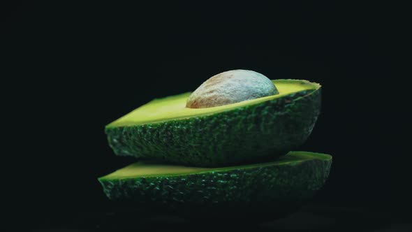Two Halves of an Avocado Rotate in a Circle on a Black Background alt