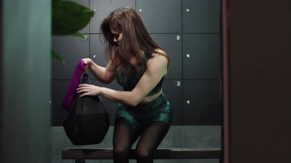 Young Pretty Woman in Sports Costume Walks in the Locker Room and Takes a Plastic Cup Out of Her Bag alt