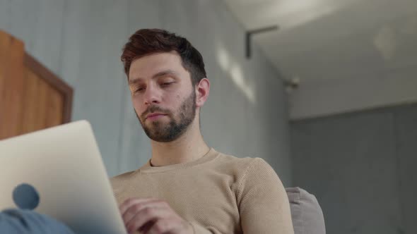 Young guy working on a laptop on the couch. Man typing with laptop on couch alt