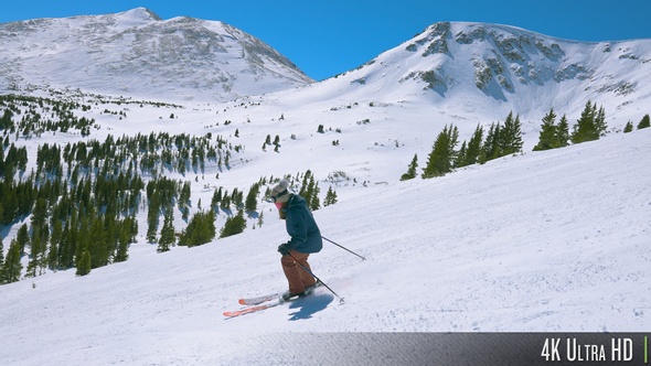 4K Slow-Motion Tracking a Downhill Skier with Snow-Capped Rocky Mountain Range in the Background alt